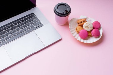 dizüstü bilgisayar ve kahve ile kadın blogger işyeri pembe arka plan üzerinde macaroons ile fincan gitmek. Üstte görüntü  