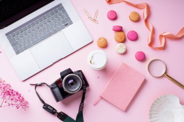 dizüstü bilgisayar ve kahve ile kadın blogger işyeri pembe arka plan üzerinde kamera ve macaroons ile fincan gitmek. Üstte görüntü 