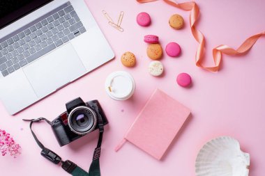 dizüstü bilgisayar ve kahve ile kadın blogger işyeri pembe arka plan üzerinde kamera ve macaroons ile fincan gitmek. Üstte görüntü 