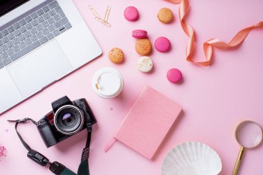 dizüstü bilgisayar ve kahve ile kadın blogger işyeri pembe arka plan üzerinde kamera ve macaroons ile fincan gitmek. Üstte görüntü 