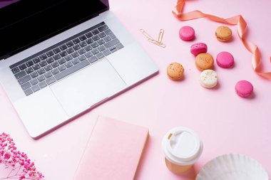 dizüstü bilgisayar ve kahve ile kadın blogger işyeri pembe arka plan üzerinde not defteri ve macaroons ile fincan gitmek. Üstte görüntü  