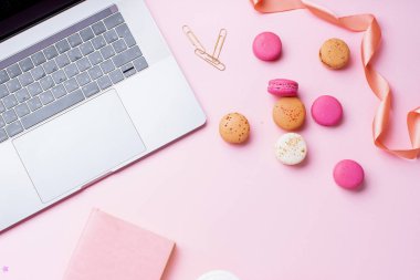 pembe arka plan üzerinde makarons ile dizüstü bilgisayar ve not defteri ile kadın blogger işyeri. Üstte görüntü  