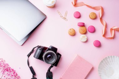dizüstü bilgisayar ve kahve ile kadın blogger işyeri pembe arka plan üzerinde kamera ve macaroons ile fincan gitmek. Üstte görüntü 