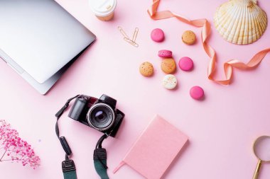 dizüstü bilgisayar ve kahve ile kadın blogger işyeri pembe arka plan üzerinde kamera ve macaroons ile fincan gitmek. Üstte görüntü 