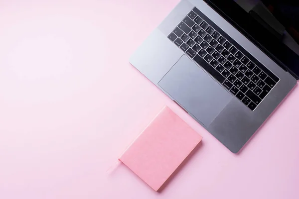 laptop with notebook on pink background. Top view, blogger workplace concept