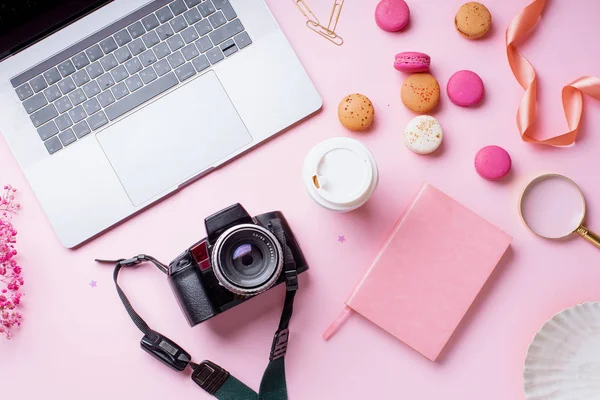 dizüstü bilgisayar ve kahve ile kadın blogger işyeri pembe arka plan üzerinde kamera ve macaroons ile fincan gitmek. Üstte görüntü 