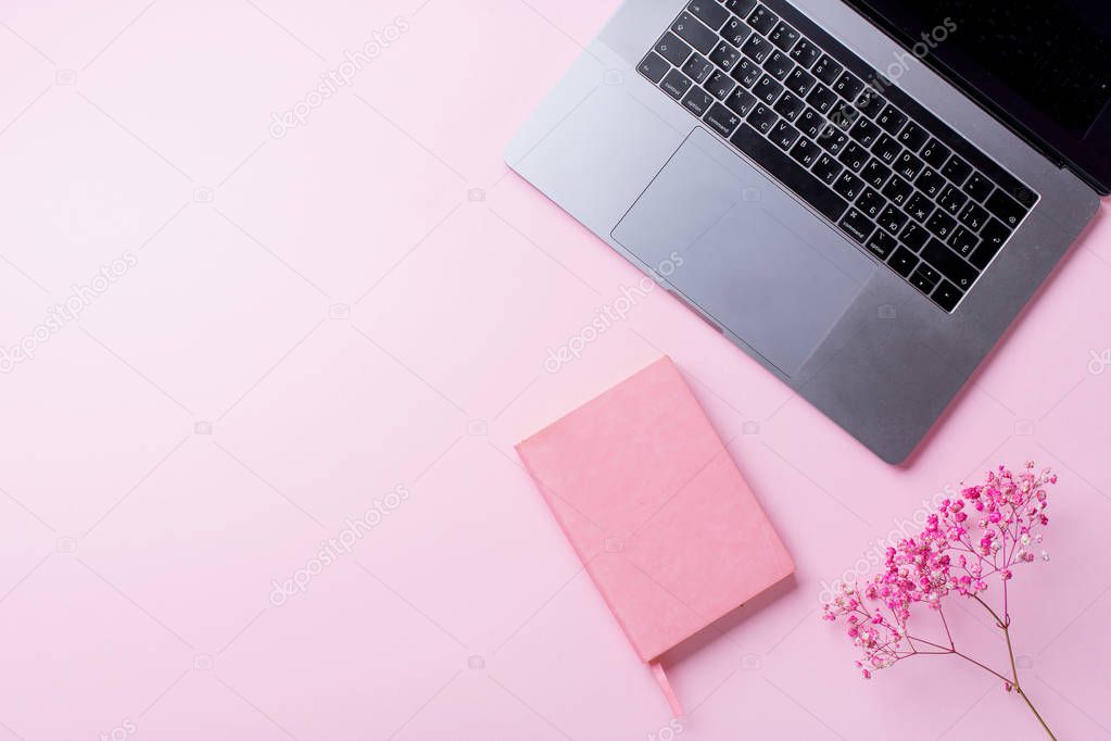 laptop with flowers and notebook on pink background. Top view, blogger workplace concept 
