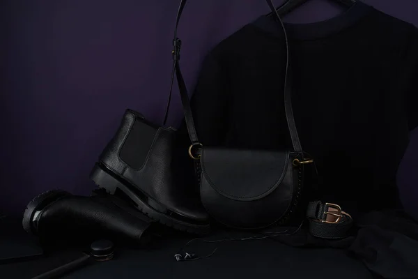 chelsea boots with leather bag and t-shirt dress arranged in dark-colored composition, close view