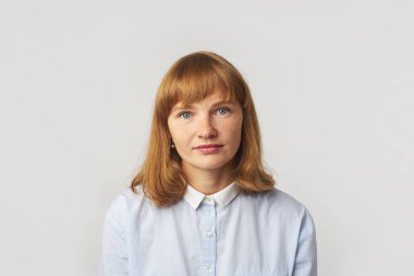 Kızıl saçlı, çilli, mavi gömlekli ve kameraya bakan genç bir kadın modelin portresi.