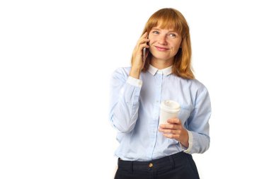 Elinde kahve fincanı olan ve beyaz arka planda izole edilmiş akıllı telefondan konuşan çilli kızıl saçlı kadının portresi.  