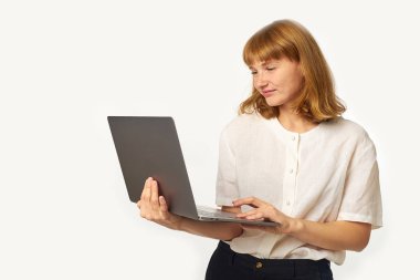 Kızıl saçlı, çilli, dizüstü bilgisayarı olan ve beyaz arka planda izole edilmiş ekrana bakan genç bir kadın. 
