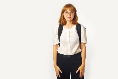 Çilli, gözlüklü, beyaz tişörtlü, büyük siyah sırt çantalı, beyaz arka planda izole kameraya bakan kızıl saçlı kadın.