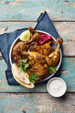 Tandoori chicken marinated in tikka served with rice naan and lime with plain yoghurt and cilantro  on wooden background. Indian cuisine concept  clipart