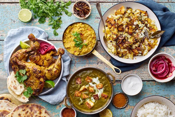 Indian cuisine dinner of tandoori chicken with biryani and red lentil curry dal with rice naan and palak paneer with basmati rice on wooden background