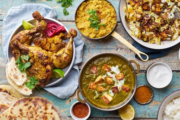 Indian cuisine dinner of tandoori chicken with biryani and red lentil curry dal with rice naan and palak paneer with basmati rice on wooden background
