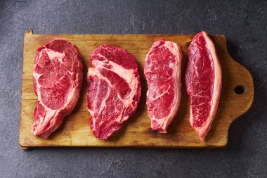 Tahtayı pirzola ve striploin ve picanha ve chuck rulo taze siyah angus ana çiğ biftek ahşap arka planda, üst görünüm