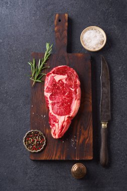 Üst Manzara: Siyah Angus bifteği. Kesme tahtasında biberiye ve çimento üzerine baharatlar. 