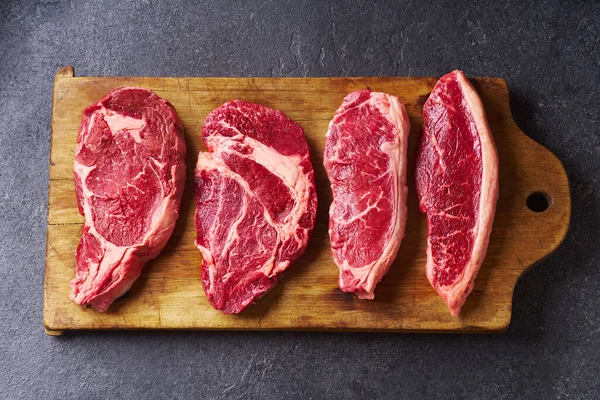 Tahtayı pirzola ve striploin ve picanha ve chuck rulo taze siyah angus ana çiğ biftek ahşap arka planda, üst görünüm