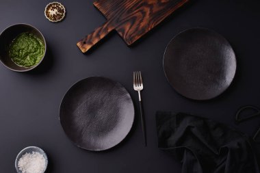 Koyu arkaplanda çatal ve ahşap kesme tahtası olan siyah boş tabaklar, akşam yemeği ayarlama şablonu   