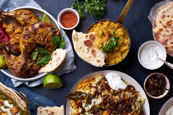 Indian cuisine dinner of tandoori chicken with biryani and red lentil curry dal with rice naan and palak paneer with basmati rice on blue background