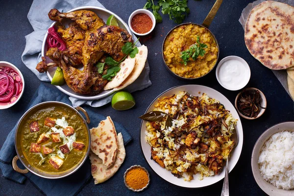 Indian cuisine dinner of tandoori chicken with biryani and red lentil curry dal with rice naan and palak paneer with basmati rice on blue background