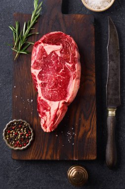 Üst Manzara: Siyah Angus bifteği. Kesme tahtasında biberiye ve çimento üzerine baharatlar. 