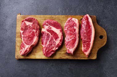 Tahtayı pirzola ve striploin ve picanha ve chuck rulo taze siyah angus ana çiğ biftek ahşap arka planda, üst görünüm
