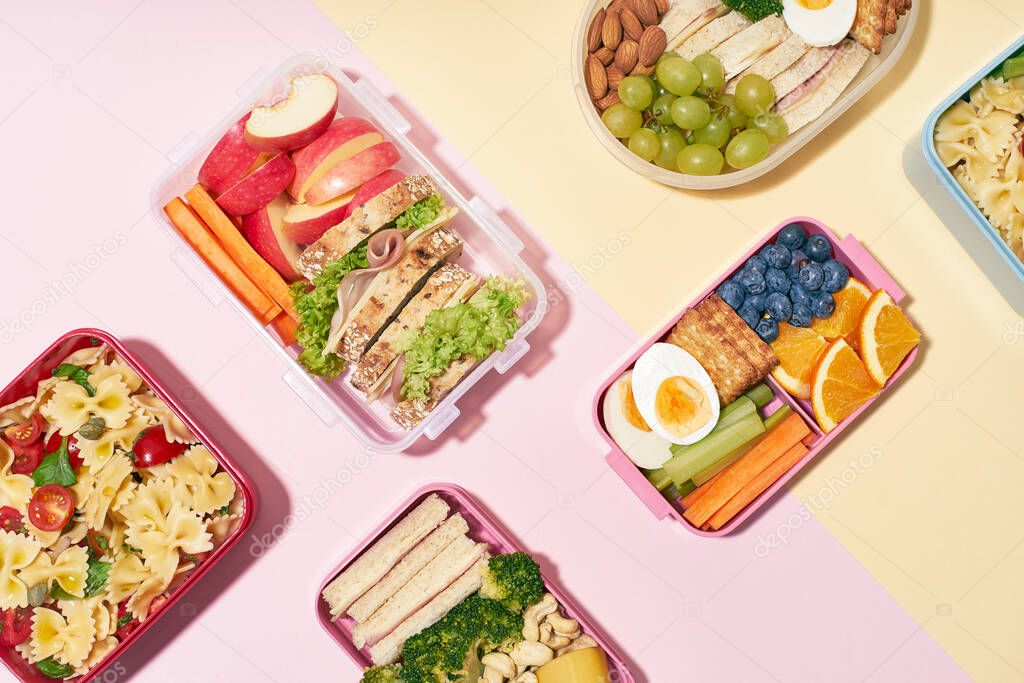 Top view of office lunchboxes with various healthy nutritious meals on pink background. Lunch food from above.