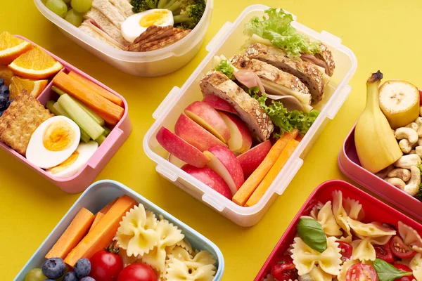 Top view pattern with office lunchboxes with various healthy nutritious meals on yellow background. Lunch food from above