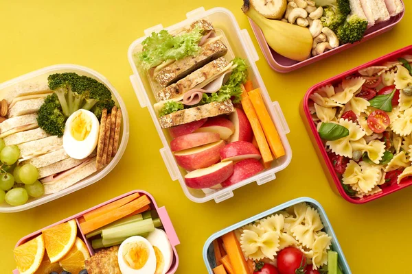 Top view pattern with office lunchboxes with various healthy nutritious meals on yellow background. Lunch food from above