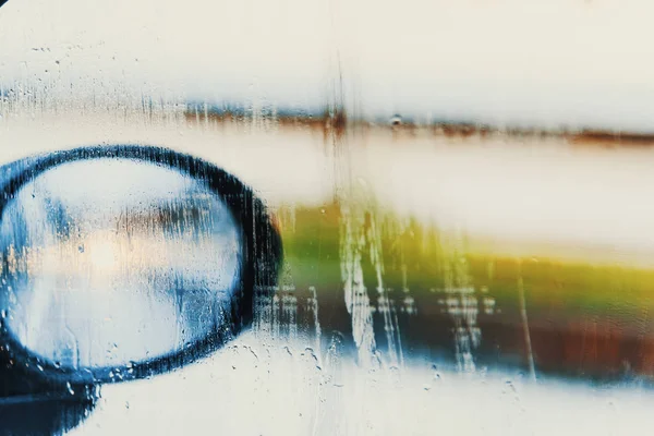 Car rearview mirror seen through a wet window — Stock Photo, Image