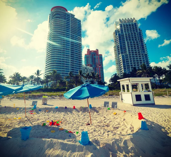 Parassóis e brinquedos de praia com arranha-céus em segundo plano — Fotografia de Stock