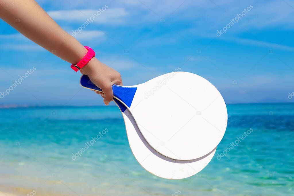 Girl holding two beach rackets with blue sea on the background