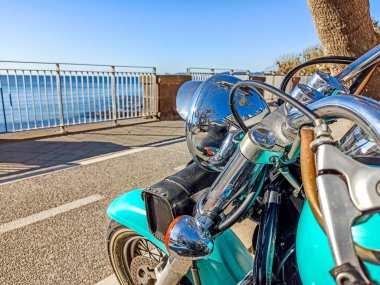 Turkuaz klasik motosiklet güneşli bir günde Alghero sahiline park edilmiş. Sardunya, İtalya