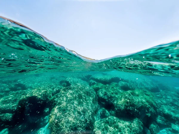 Split underwater view of a rocky sea bed under a blue sky