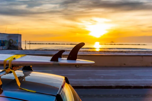 Surfboard on a car rooftop by the sea at sunset