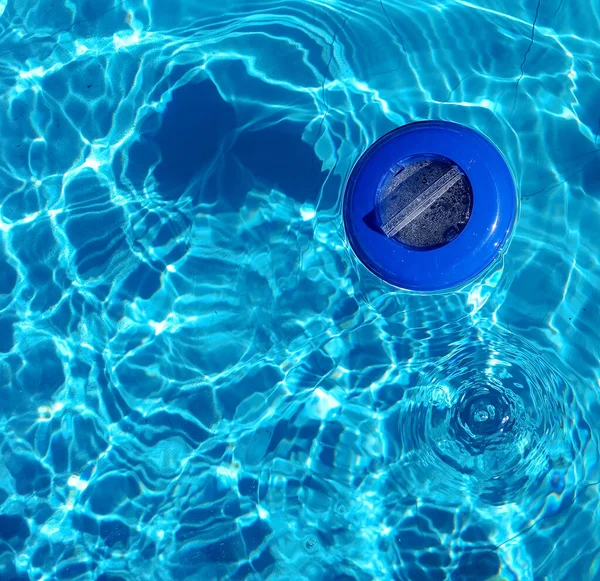 Plastic chlorine dispenser and blue water seen from above. Chlorine dispenser is used to disinfect the swimming pool's water