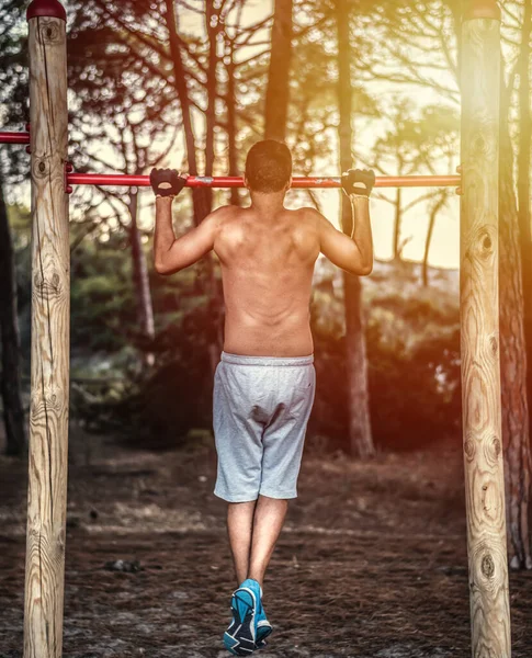 Man doing pull ups in a park at sunset
