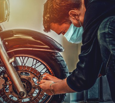 Virüs koruyucu maskeli motorcu klasik bir motorsikletin frenini kilitliyor