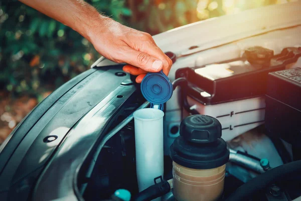 Close up of a man opening the windshield washer fluid tank of an suv