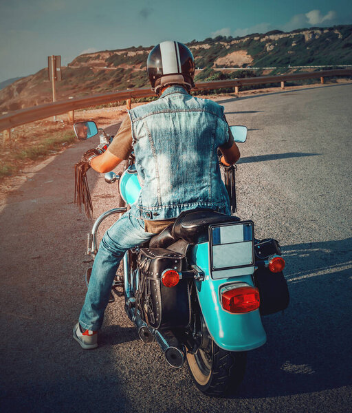Biker on a turquoise classic motorcycle seen from below at sunset