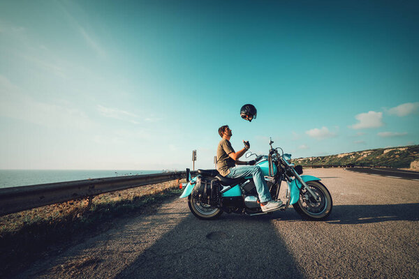 Biker on a classic motorcycle tossing the helmet in the air at sunset