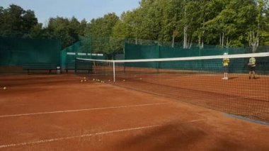 Kırmızı tenis kortu üzerinde eğitim genç tenisçiler, ön planda tenis net