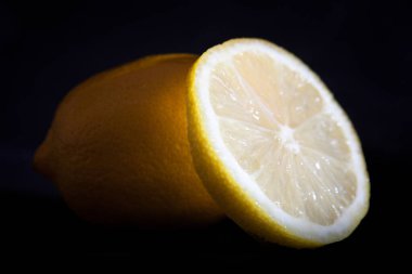 Bütün bir limonu ve siyah arka plandaki dilimini gösteren bir stüdyo fotoğrafı.