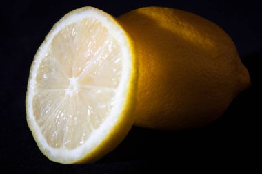 Bütün bir limonu ve siyah arka plandaki dilimini gösteren bir stüdyo fotoğrafı.