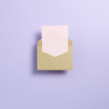 Açık mor zemin üzerinde Kraft zarf ve boş kart. Üst görünüm, boşluk kopyala