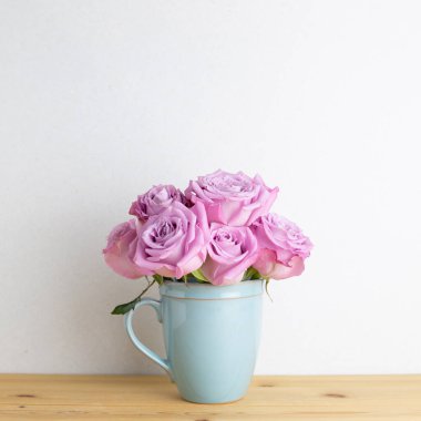 Beyaz arkaplanlı ahşap masada, fincanda mor gül çiçekleri. Boşluğu kopyala