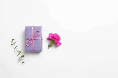 Beyaz arka planda karanfil çiçeği olan mor hediye kutusu. düz alan, üst görünüm, kopyala boşluk