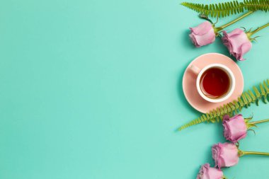 Nane yeşili arka planda pembe gül çiçekli siyah çay. Çiçek kompozisyonu, düz konum, üst görünüm, kopyalama alanı