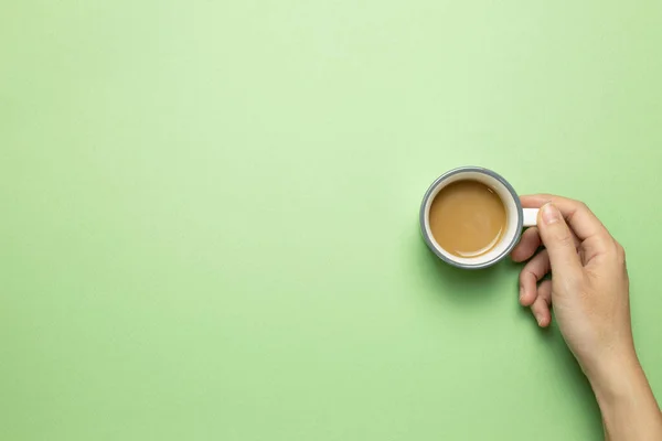 Hand holding cup of coffee on green background. top view, copy space
